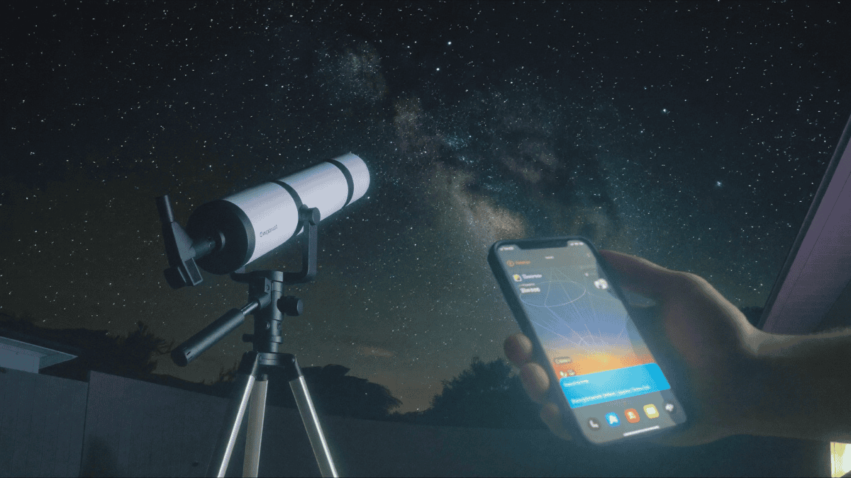 A compact smart telescope with a glowing tablet under a starry suburban sky