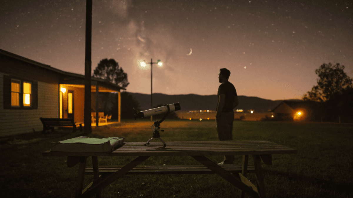 Backyard astronomer beside a tabletop telescope under a light-polluted suburban sky