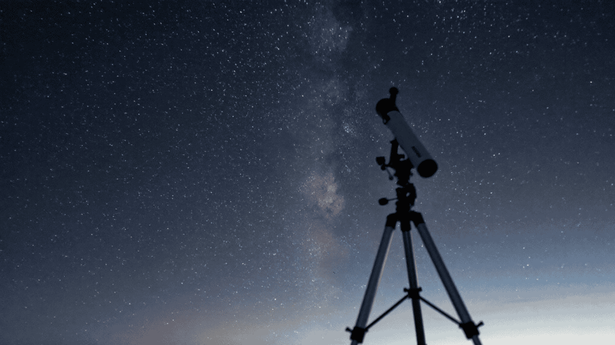 A small refractor telescope silhouetted against a star-filled twilight sky