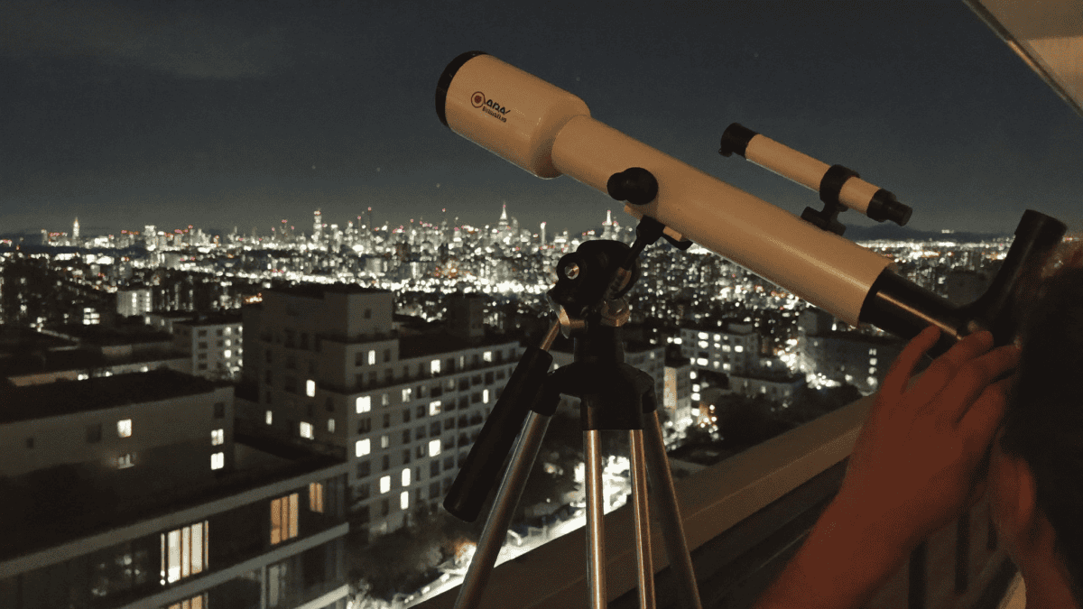A small telescope on an apartment balcony at night with city lights in the background