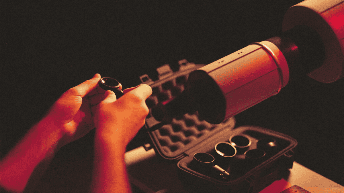 Amateur astronomer changing a telescope eyepiece at night with an eyepiece case nearby