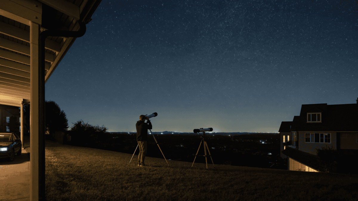 Amateur astronomer with a telescope in a suburban backyard at night under light-polluted skies