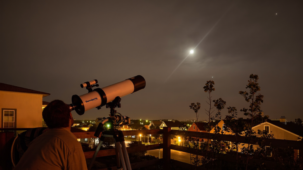 Backyard telescope on a suburban patio under an orange light-polluted sky with a few bright stars visible