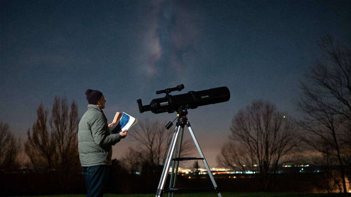 Amateur astronomer standing beside a Dobsonian telescope under a suburban night sky with a star chart, observing Messier objects
