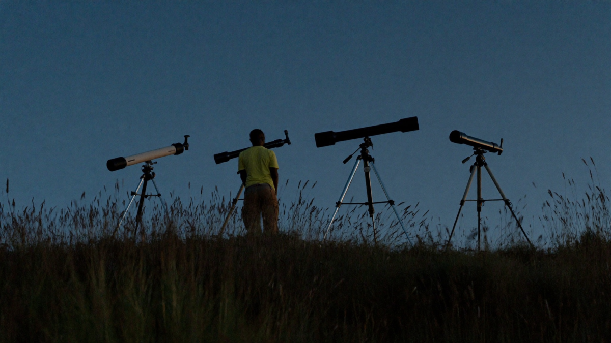Three different telescope types silhouetted on a hilltop against a starry twilight sky