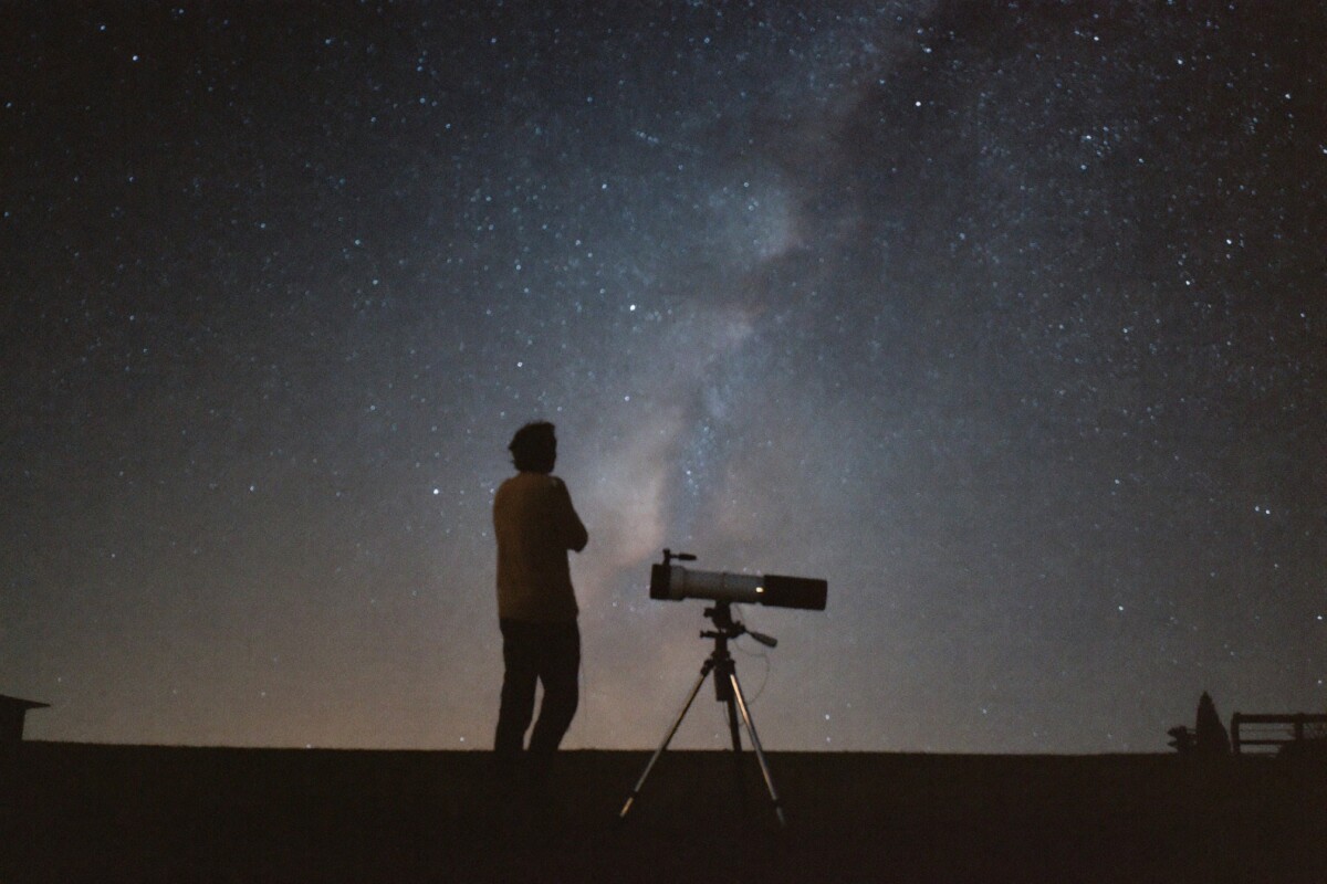 Amateur astronomer silhouetted beside a telescope on a lawn under a star-filled sky with the Milky Way visible